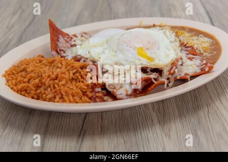 I chilaquiles, coperti di uova fritte e serviti su un piatto con riso, e fagioli per un pasto messicano molto abbondante. Foto Stock