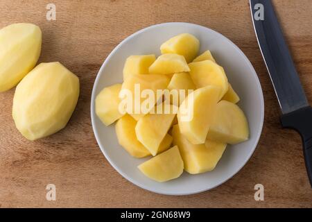patate crude tritate su un piatto bianco, con un coltello e patate sbucciate intere sullo sfondo, vista dal primo piano presa dall'alto Foto Stock