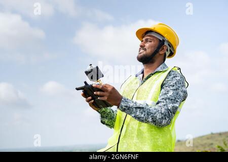 Pilota drone con elmetto di sicurezza che utilizza il drone con telecomando - concetto di ingegnere che utilizza la tecnologia dei droni per il rilevamento del terreno. Foto Stock