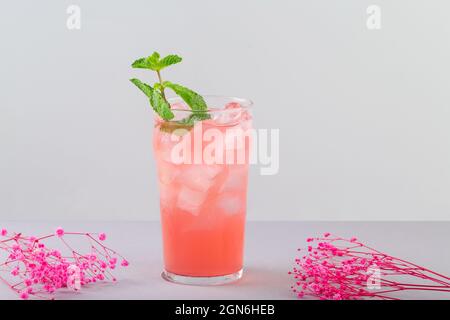 rinfrescante cocktail rosa con sciroppo d'uva e fiori di menta rosa accanto al bicchiere grigio Foto Stock