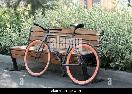 Orizzontale non si spara la gente di bicicletta moderna parcheggiata all'aperto contro panca di legno nel parco della città il giorno d'estate Foto Stock