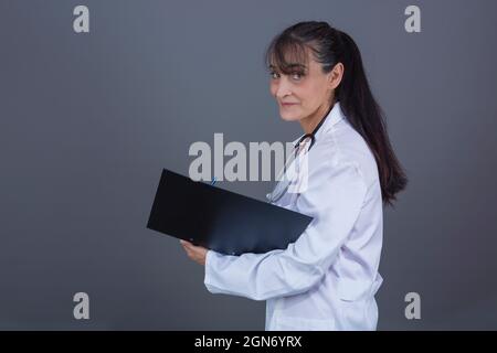 bella donna caucasica dottore nel suo 40s con i capelli lunghi cartella in mano, lato di fronte alla macchina fotografica. Foto Stock
