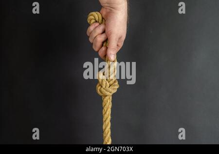 Maschio adulto tiene verticalmente una corda con un nodo. La mano tiene uno yel Foto Stock