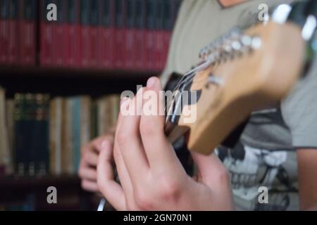 Un ragazzo che suona la chitarra elettrica. Foto ravvicinata della mano che preme sulle corde della chitarra elettrica. Identità non riconoscibile, sfondo sfocato. Foto Stock