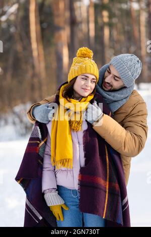 Uomo sorridente che indossa una coperta sulla ragazza nel parco invernale Foto Stock