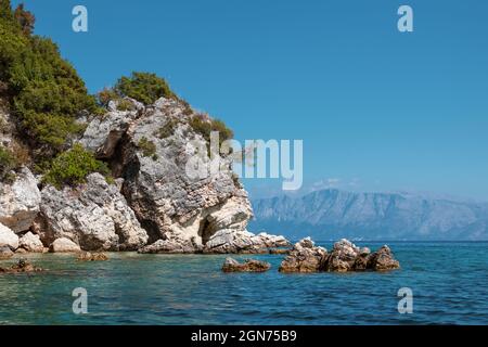 Rocce panoramiche nelle acque blu del Mar Ionio con scogliere rocciose, montagne distanti e cielo luminoso. Natura dell'isola di Lefkada in Grecia. Estate in affitto Foto Stock