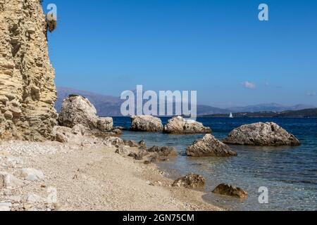 Ciottoli bianchi e rocce scogliere spiaggia con acque azzurre limpide e montagne in lontananza sulla costa dell'isola di Lefkada in Grecia. Estate natura selvaggia vacatio Foto Stock