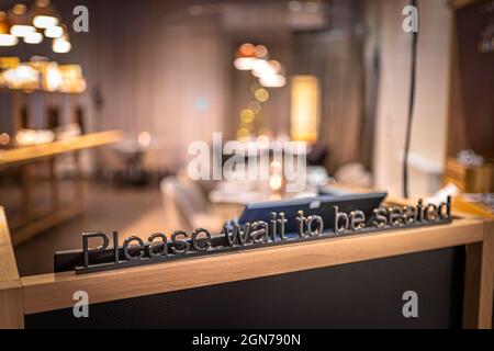 Attendere di essere seduti in metallo segno nel ristorante Foto Stock