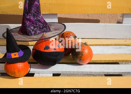 zucche arancioni su una panca di legno. alcune delle zucche in cappelli di strega e una maschera protettiva nera. Decorazioni di strada per Halloween in nuova realtà di Foto Stock