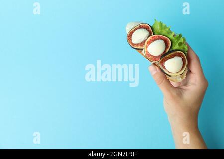 La mano femmina tiene la bruschetta con il fico su sfondo blu Foto Stock