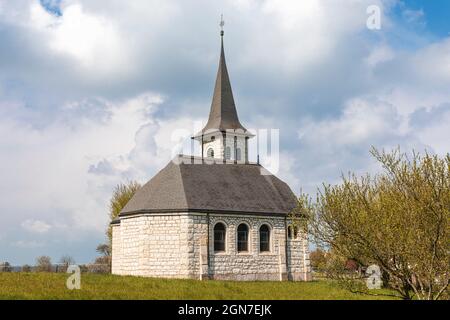 Chiesa caratteristica nel campo verde delle Alpi svizzere del Cantone Giura. Nessuno dentro. Giorno nuvoloso. Foto Stock