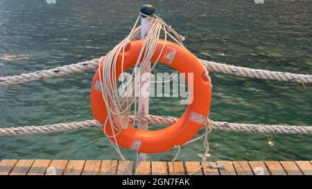 Linea di salvezza arancione e corde di mare sullo sfondo del mare e cielo blu. Funi marine e salvagente appesi su un palo. Concetto di aiuto e sicurezza Foto Stock