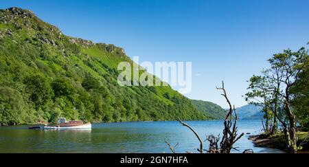 Lungo la West Highland Way in Scozia. Una vista del Loch Lomond che mostra alcuni ceppi di alberi e una vecchia barca a motore in una giornata di sole Foto Stock