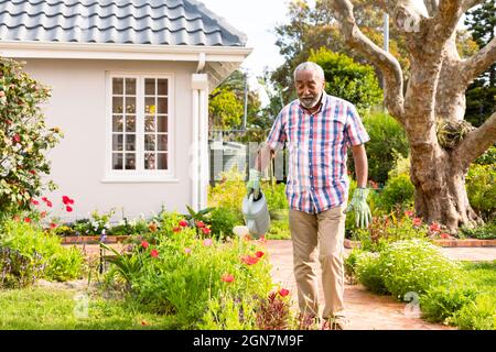 African american Senior Man annaffiatura piante in cortile Foto Stock