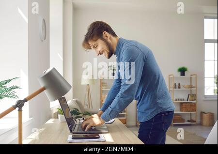 Felice giovane uomo d'affari o freelance che scrive il testo sul notebook mentre lavora a casa. Foto Stock