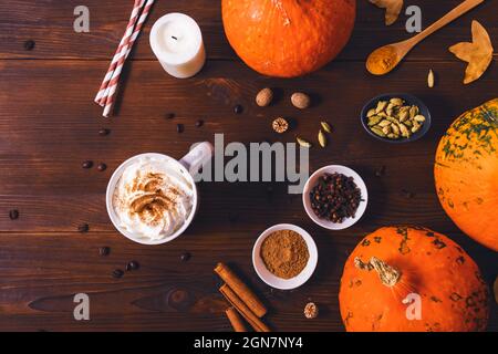 Latte di zucca speziata in tazza con panna montata accanto agli ingredienti e candela su tavola di legno scuro, vista dall'alto Foto Stock