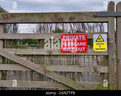 Cartelli su un cancello di legno da cortile avvertano che l'area è un terreno agricolo privato e che l'ingresso è vietato. Un segno in giallo avverte che la sicurezza TVCC è in uso. Foto Stock