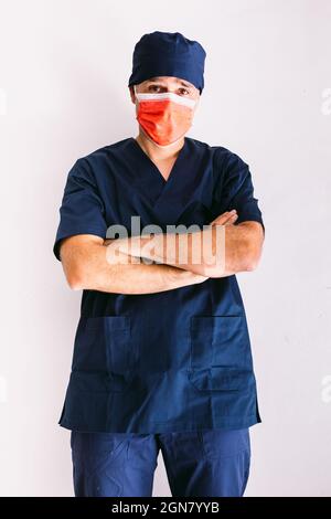 Infermiera maschile, medico o veterinario con maschera rossa e uniforme blu scuro in ospedale, braccia incrociate, sorridente. Concetto di medicina, ospedale e assistenza sanitaria. Foto Stock