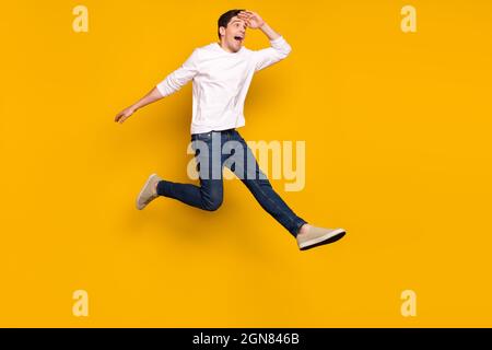 Foto a tutta lunghezza del profilo di impressa brunetta giovane ragazzo salto look indossare camicia jeans sneakers isolato su sfondo giallo Foto Stock