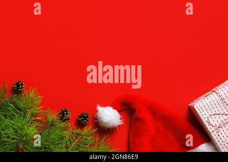 Composizione di Natale da una scatola regalo, rami di abete rosso, cappelli di Santa su sfondo rosso. Spazio di copia con vista dall'alto in posizione piana Foto Stock