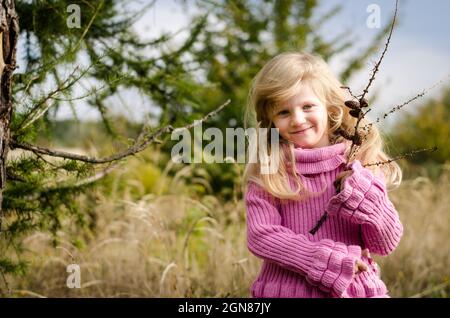 piccola bella ragazza con capelli biondi lunghi sorridenti in autunno foresta Foto Stock