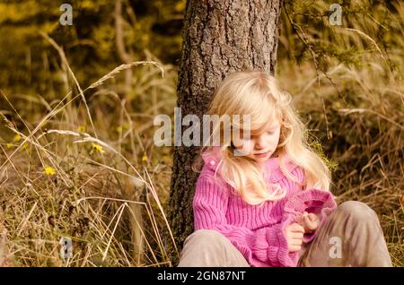 piccola bella ragazza con capelli biondi lunghi sorridenti in autunno foresta Foto Stock