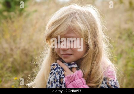 piccola ragazza bella con lunghi capelli biondi che piangono da sola in autunno natura Foto Stock