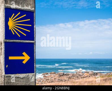 MUXIA, SPAGNA - 08 ago 2021: L'immagine mostra un cartello con simboli della via di San Giacomo con il mare e il cielo blu sullo sfondo Foto Stock