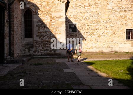 Aquileia, italia - Agosto 15: Due turisti che camminano accanto alla Basilica di Santa Maria Assunta il 15 Agosto 2021 Foto Stock