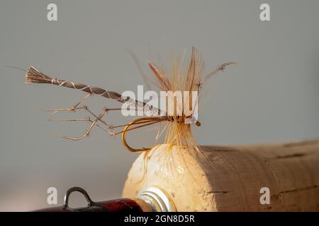 fuoco selezionato del punto di gancio di una mosca da pesca artificiale che penetra un manico di sughero di una canna da pesca Foto Stock