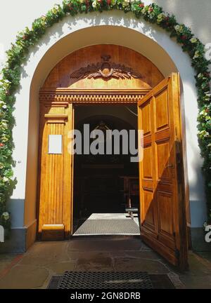 Scatto luminoso verticale di una porta di legno ad arco aperta che conduce ad una chiesa circondata da fiori Foto Stock