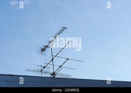 Antenna per la ricezione di programmi televisivi su un tetto di tegole grigie contro un cielo blu Foto Stock