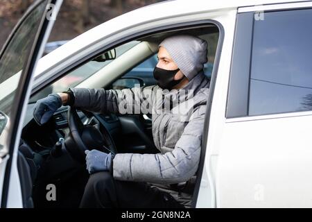 Il colpo orizzontale dell'uomo indossa occhiali e maschera medica protettiva per il viso, si trova vicino all'auto, si sposta per lavorare con il trasporto personale durante la quarantena Foto Stock