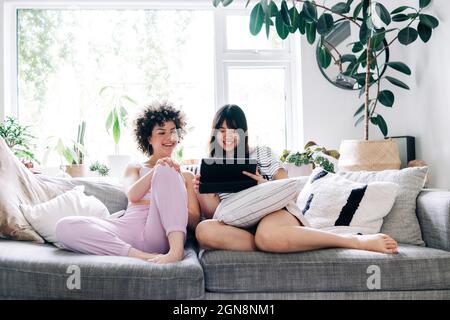 Le giovani donne che usano il tablet digitale mentre si siedono sul divano Foto Stock