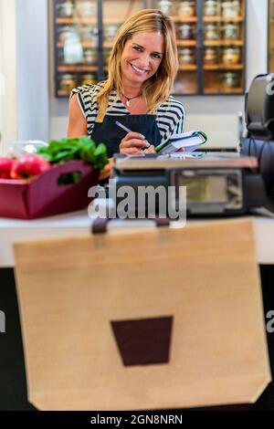 Sorridente cassiere femmina al banco cassa Foto Stock