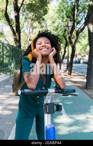 Sorridente giovane donna appoggiata su uno scooter elettrico a spinta Foto Stock