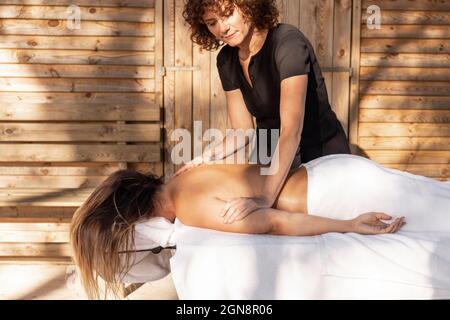 Massaggiatrice femminile che applica l'olio sul corpo della donna di fronte alla cabana Foto Stock