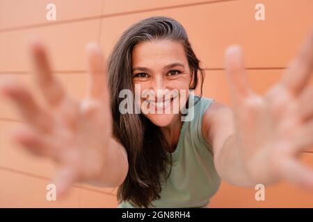 Sorridente bella donna matura che raggiunge con le braccia tese Foto Stock