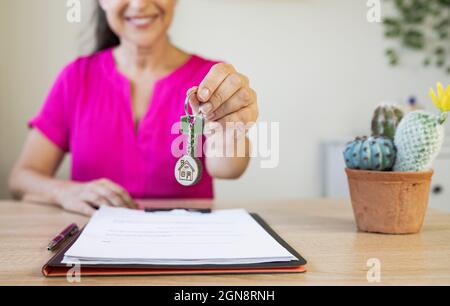 Sorridente agente immobiliare femminile che dà la chiave della casa in ufficio a casa Foto Stock