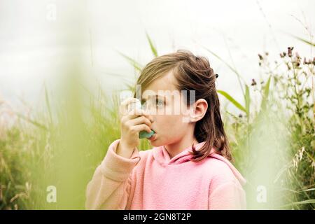 Ragazza con cappuccio rosa usando l'inalatore per asma Foto Stock