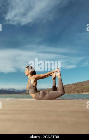 Giovane donna che pratica Dhanurasana sul molo Foto Stock