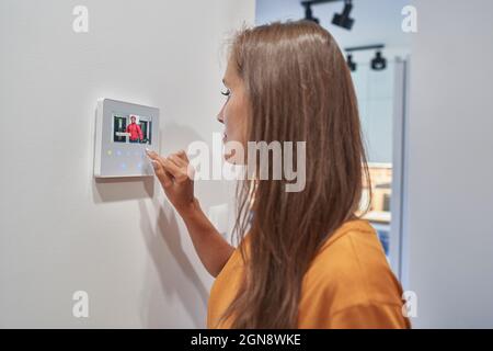 Donna che guarda la persona di consegna della pizza sul dispositivo di automazione domestica Foto Stock