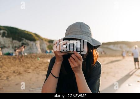 Giovane donna che fotografa con la macchina fotografica in spiaggia Foto Stock