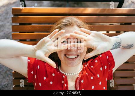 Felice giovane donna che copre il viso mentre si trova sulla poltrona Foto Stock