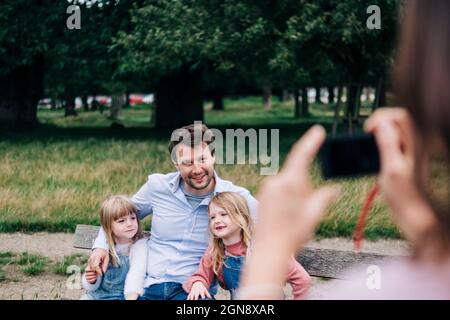 Donna che fotografa uomo e ragazze attraverso la macchina fotografica al parco Foto Stock