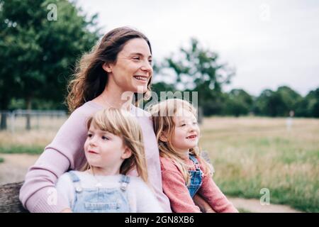 Madre sorridente seduta con le figlie al parco pubblico Foto Stock