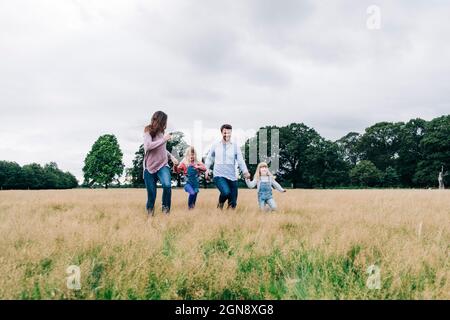 I genitori tengono le mani delle figlie mentre corrono sul prato Foto Stock