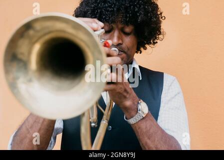 Uomo che gioca tromba di fronte al muro beige Foto Stock