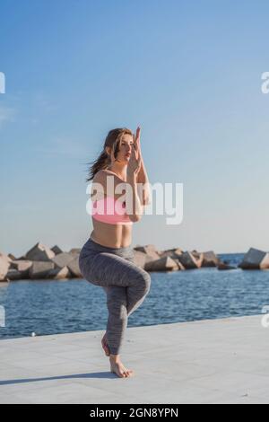 Giovane donna che pratica Garudasana sul lungomare Foto Stock