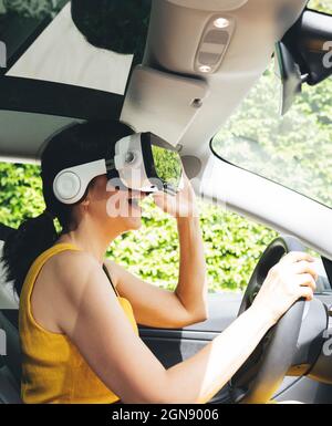Donna che indossa un simulatore di realtà virtuale mentre guida un'auto elettrica Foto Stock